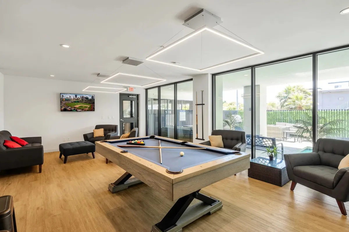 A vibrant community lounge featuring a pool table, plush lounge seating, a large TV screen, and expansive windows letting in natural light. The space is designed for casual recreation and relaxed social gatherings, with comfortable furnishings and modern decor.