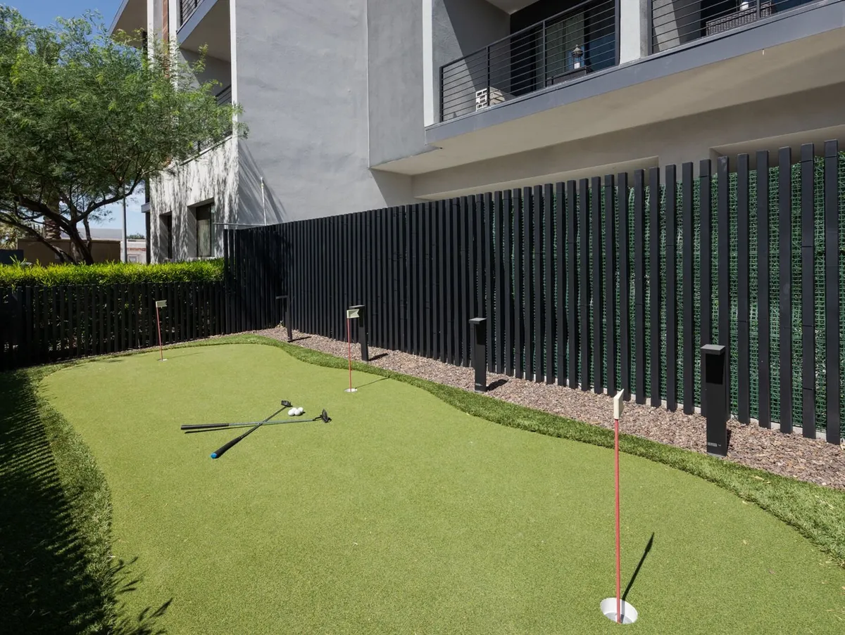 A modern outdoor putting green bordered by attractive landscaping and contemporary fencing, with a backdrop of the property’s sleek architecture. The space encourages playful competition and casual outdoor gatherings.