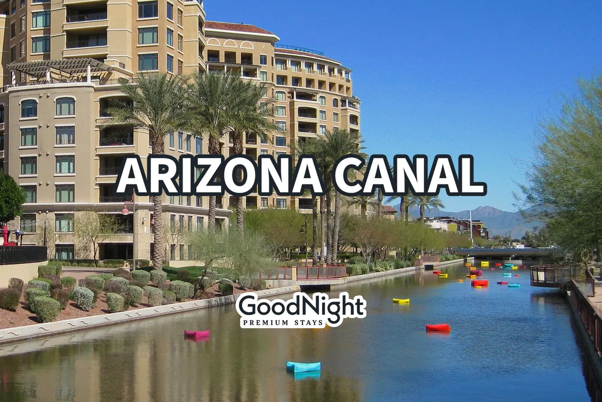 The Arizona Canal winds through Old Town, with colorful boats floating on the water, palm trees lining the banks, and vibrant residential buildings nearby. People can be seen enjoying boating and relaxing by the lively waterfront.