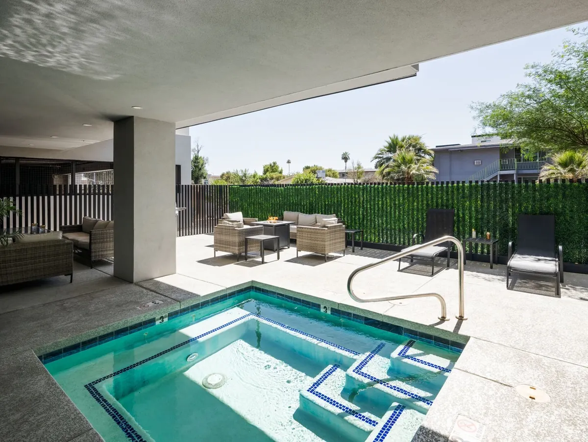 An inviting outdoor area with a bubbling jacuzzi surrounded by lush greenery and a fence, featuring ample seating for relaxation. The setting is serene and perfect for unwinding, with the added appeal of sunset views for a luxurious soak.